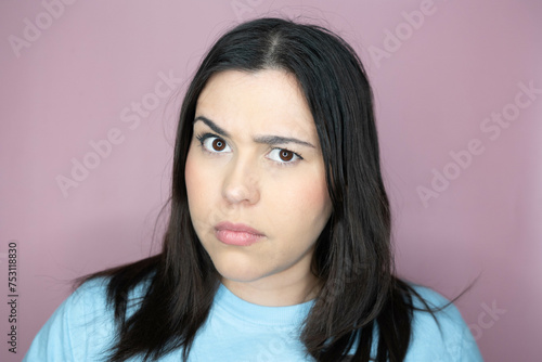Close up image of an attractive young woman with long hair and a playful look, making an amused expression ina pink background