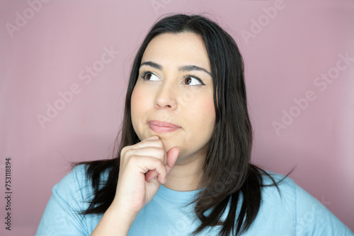 Close up image of an attractive young woman with long hair and a playful look, making an amused expression ina pink background