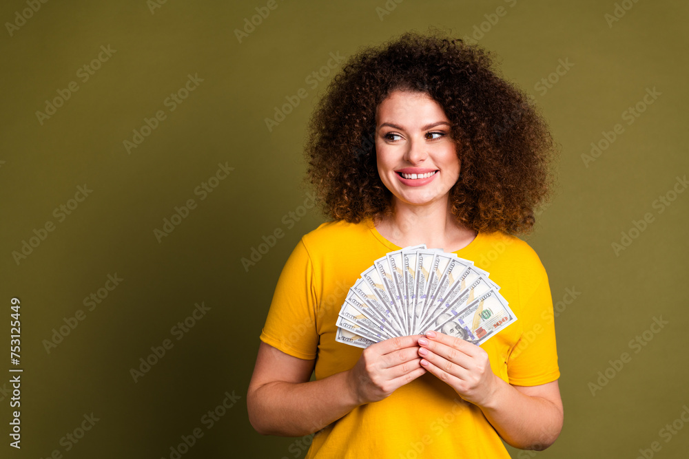 Photo of young positive curly woman in yellow t shirt holding money saving looking empty space dream isolated on khaki color background Photo of young positive curly woman in yellow t shirt holding money saving looking empty space dream isolated on khaki color background