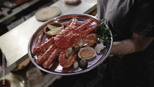 Seafood and gastronomy. Top view of a waitress holding a tray with a fresh King Crab dish in the kitchen.
