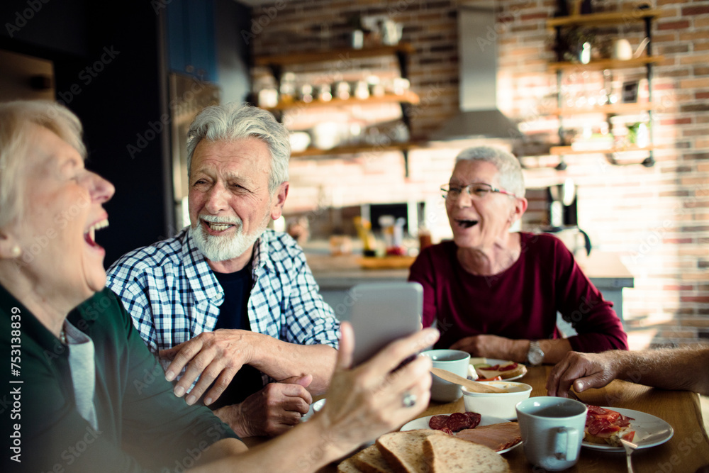 Group of happy seniors enjoying breakfast and using smartphone together Group of happy seniors enjoying breakfast and using smartphone together