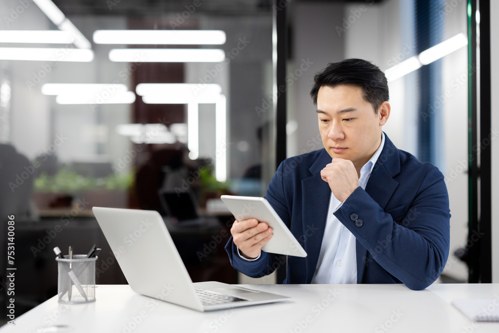 A professional businessman thoughtfully using a digital tablet, with a laptop open in his well-lit office space. A professional businessman thoughtfully using a digital tablet, with a laptop open in his well-lit office space.