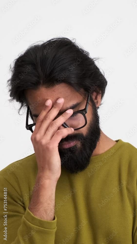 Depressed bearded young man with eyes closed shaking and touching his head in pain while standing isolated against white background Depressed bearded young man with eyes closed shaking and touching his head in pain while standing isolated against white background