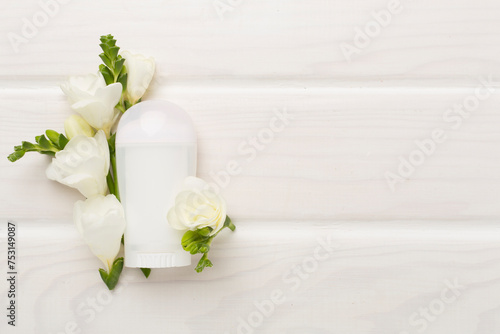 Cosmetic bottle with freesia flowers on wooden background, top view