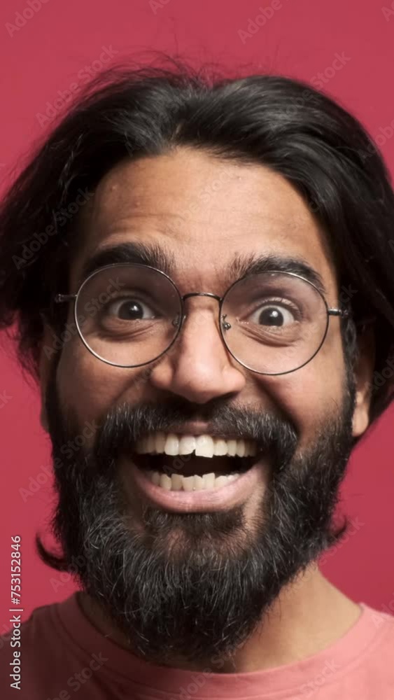 Closeup portrait of bearded surprised young man screaming and shaking hands while celebrating victory against isolated red background Closeup portrait of bearded surprised young man screaming and shaking hands while celebrating victory against isolated red background