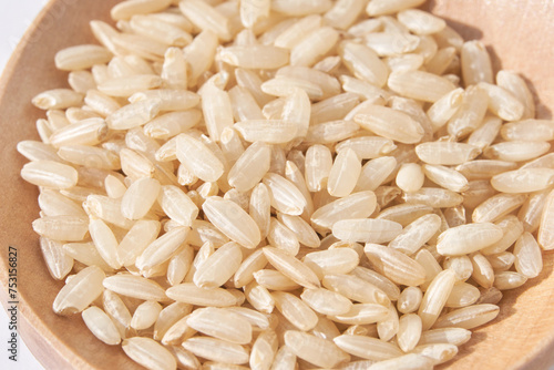 A closeup of long, uncooked brown rice grains on a wooden spoon surface, emphasizing the healthy, natural aspect of this whole food. Pile gluten texture