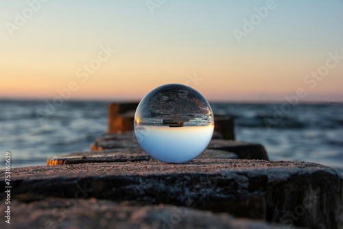 The beach and sea are reflected in a glass ball that lies on a wooden breakwater © Claudia Evans 