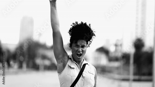 One determined young black woman raises fist in the air feeling empowered in dramatic black and white. African American female 20s person showing solidarity for cause photo