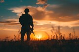 A Silhouette of a soldier stands in a field at sunset, holding his rifle. 