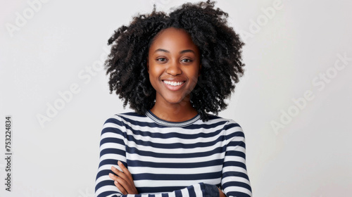 young woman with curly afro hair, wearing a striped shirt, standing with her arms crossed, smiling and looking directly at the camera © MP Studio