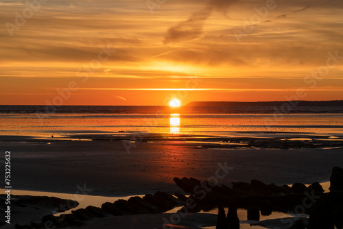 Le coucher de soleil embrase une plage de la Presqu'île de Crozon, Bretagne, offrant un spectacle enchanteur où le ciel et la mer se fondent dans des teintes dorées. photo