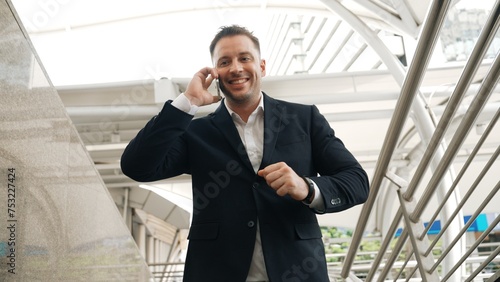 Skilled businessman receive good news for getting promotion while walking at corridor. Happy smart manager calling or talking to telephone with marketing team for increasing sales. Lifestyle. Urbane.