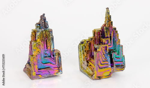 Beautiful colored brittle bismuth hopper crystals with stairstep structure on white background. Two heavy metal pieces of diamagnetic chemical element Bi with rainbow oxidised surface. Used in alloys.