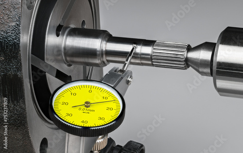 Closeup a shaft run-out measurement by yellow dial test indicator with metal probe on hinge and round tip. Precise mechanical tool at measuring runout of steel rotor of rotary vane compressor of pump.