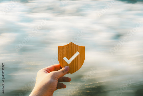 Life insurance businessman with bang holding wooden shield symbol with check mark with a background of fast-flowing water, it indicates an uncertain future.