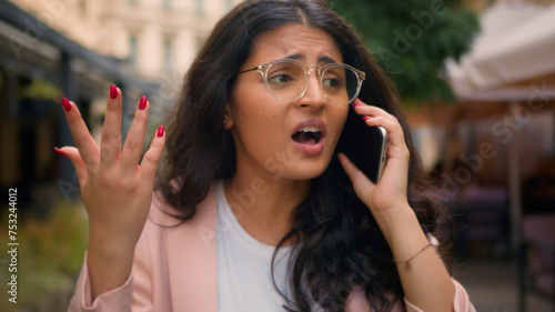Mad angry stressful Indian Arabian ethnic woman businesswoman lady female walking city street yell talking arguing mobile phone business telephone cellphone call conversation discuss conflict outside