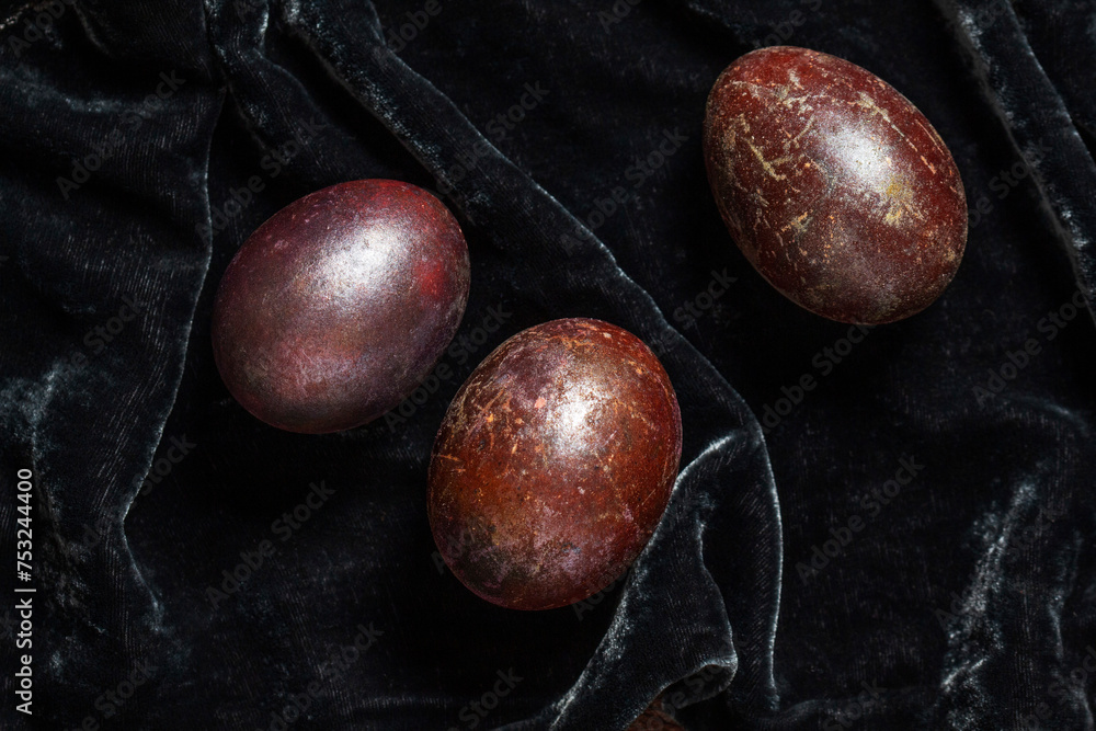 Eggs stained with wine and covered with mother-of-pearl on a dark velvet background. Easter concept.