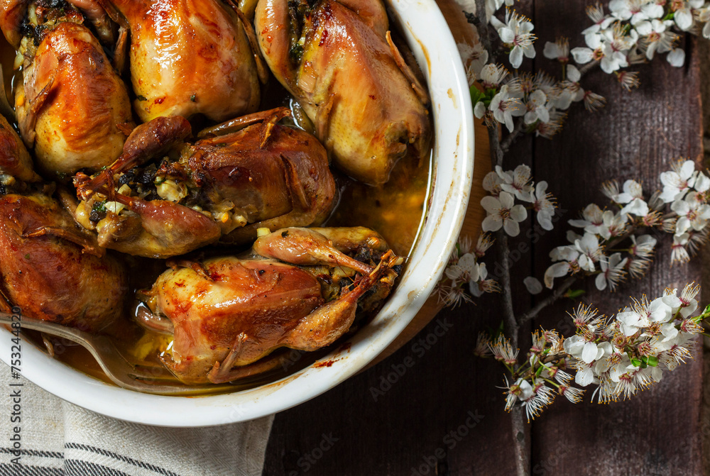 Baked quail stuffed with mushrooms, eggs and bread in a ceramic form on a wooden table.