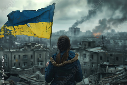 A woman holding Ukraine flag in a city with smoke in the background. The flag is torn and dirty photo
