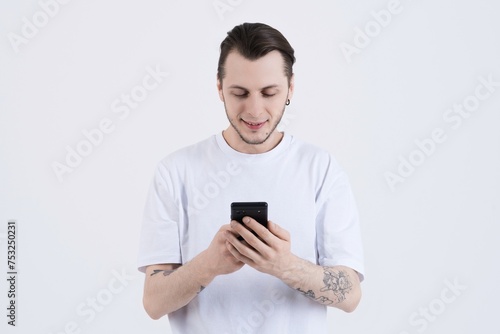 Attractive caucasian young man with tattoos in casual clothes using mobile phone isolated on white studio background. Technology, Freelancing, Wireless. © Павел Костенко