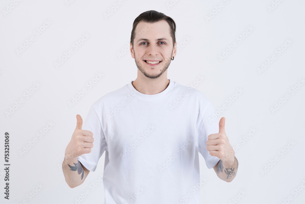 Attractive caucasian young man with tattoos in casual clothes looking at camera, smiling and showing thumbs up isolated on white studio background Attractive caucasian young man with tattoos in casual clothes looking at camera, smiling and showing thumbs up isolated on white studio background