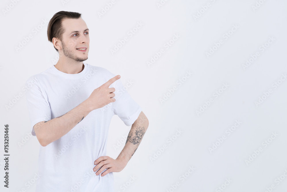 Attractive caucasian young man with tattoos in casual clothes smiling and pointing finger at blank copy space for advertising isolated on white studio background Attractive caucasian young man with tattoos in casual clothes smiling and pointing finger at blank copy space for advertising isolated on white studio background