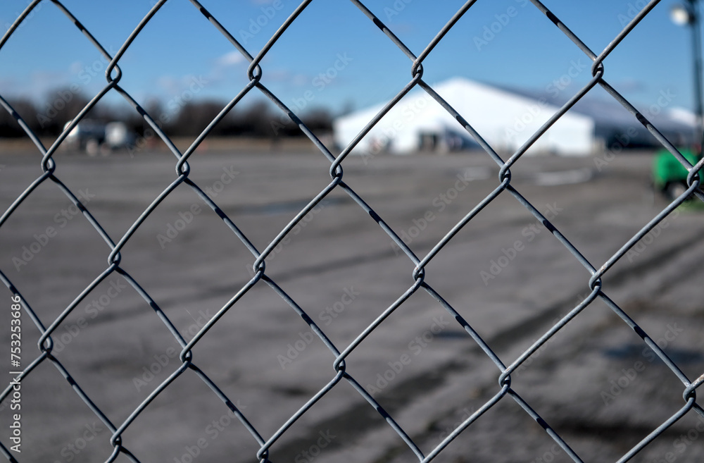 white tent behind a metal fence (out of focus large facility seen through chain link fencing) at abandoned airstrip in floyd bennett field, brooklyn, new york city white tent behind a metal fence (out of focus large facility seen through chain link fencing) at abandoned airstrip in floyd bennett field, brooklyn, new york city