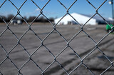 white tent behind a metal fence (out of focus large facility seen through chain link fencing) at abandoned airstrip in floyd bennett field, brooklyn, new york city