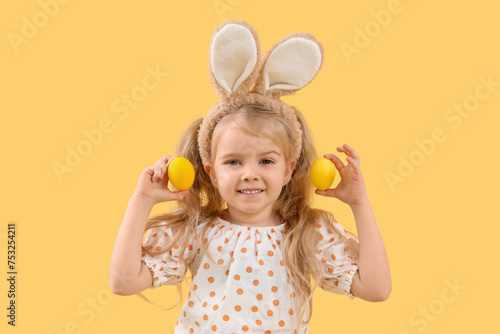 Cute little girl with bunny ears and Easter eggs on yellow background