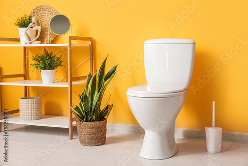 Interior of stylish bathroom with houseplants and ceramic toilet bowl near orange wall © Pixel-Shot