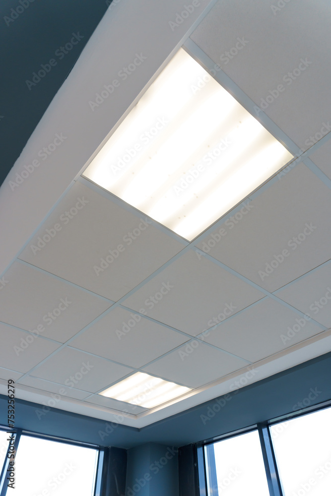 Fototapeta premium Square lamp on a white office ceiling. Interior design in the office. A fluorescent lamp on a modern suspended ceiling.
