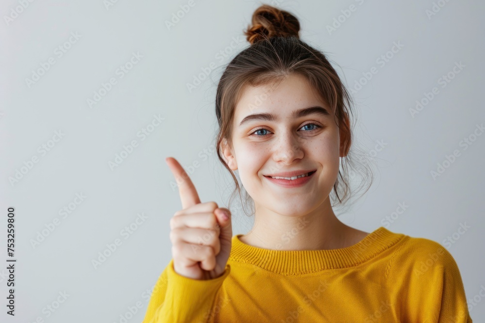 A young woman in a yellow sweater was holding up a finger. He has blue eyes and a smile on his face A young woman in a yellow sweater was holding up a finger. He has blue eyes and a smile on his face
