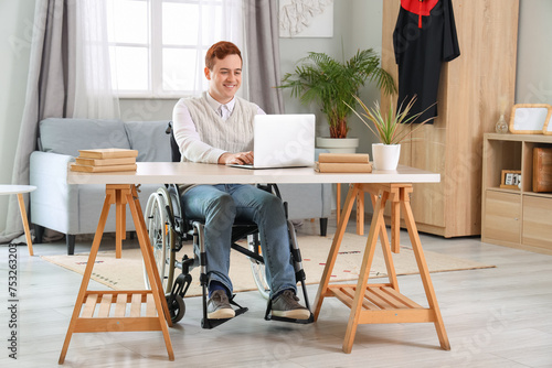 Male graduate in wheelchair using laptop at home © Pixel-Shot