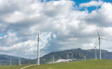 Renewable energy concept with windmills on a grassy field against a cloudy sky