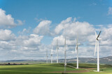 Wind turbines standing in rolling green hills under a cloudy sky for sustainable energy production