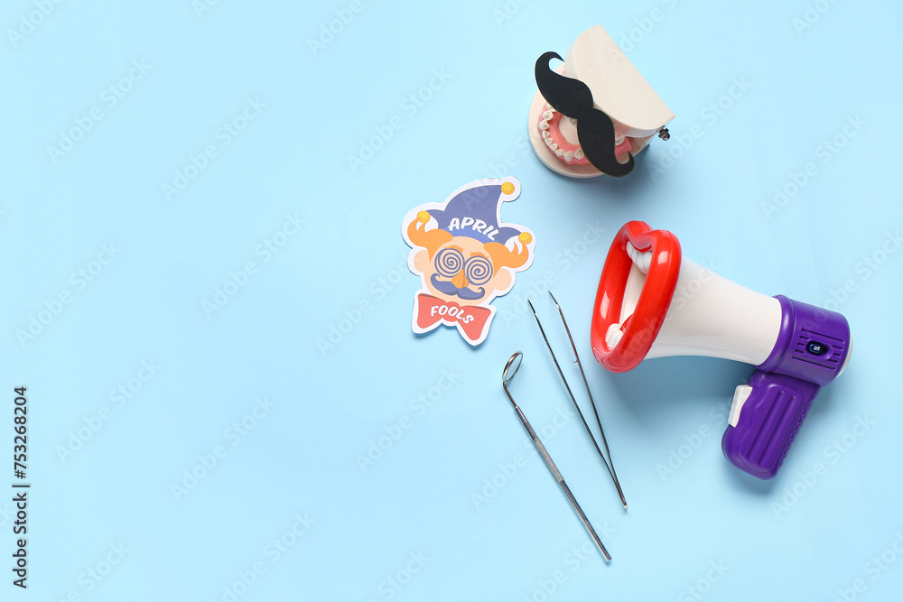 Model of jaw with paper mustache, megaphone and dentist tools on blue background. April Fools Day - obrazy, fototapety, plakaty 