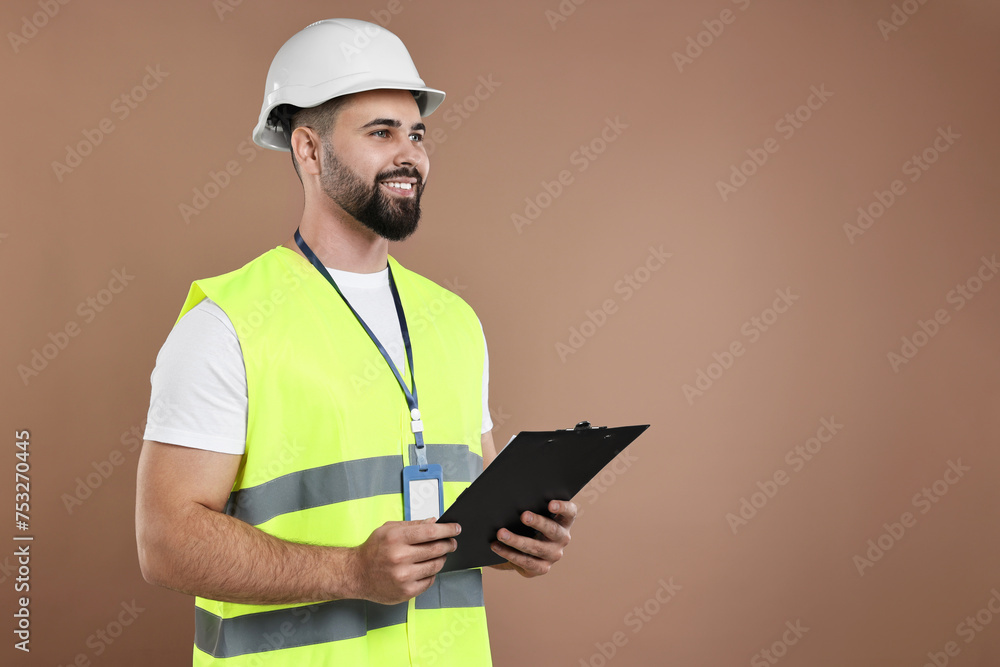 Engineer in hard hat holding clipboard on brown background, space for text Engineer in hard hat holding clipboard on brown background, space for text