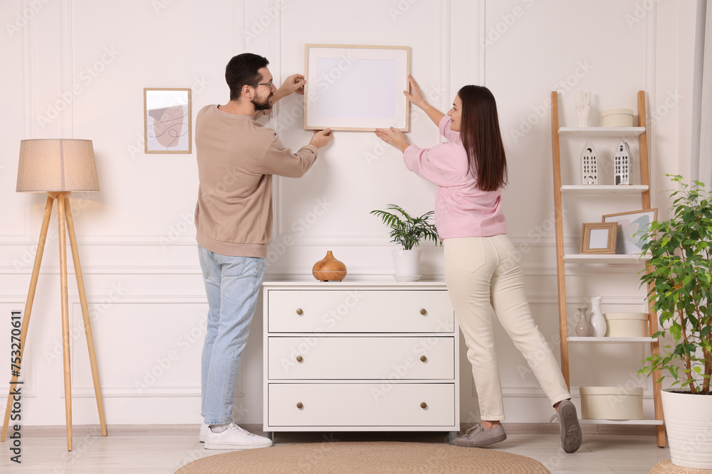 Man and woman hanging picture frame on white wall at home Man and woman hanging picture frame on white wall at home
