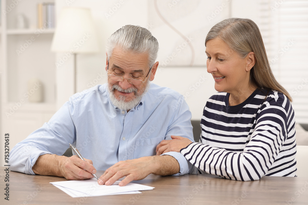 Happy senior couple signing Last Will and Testament indoors Happy senior couple signing Last Will and Testament indoors