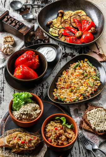 Different healthy vegan food, eggplant caviar, grilled zucchini, stuffed bell peppers and rice with vegetables on wooden background. Healthy vegetarian food, top view, flat lay
