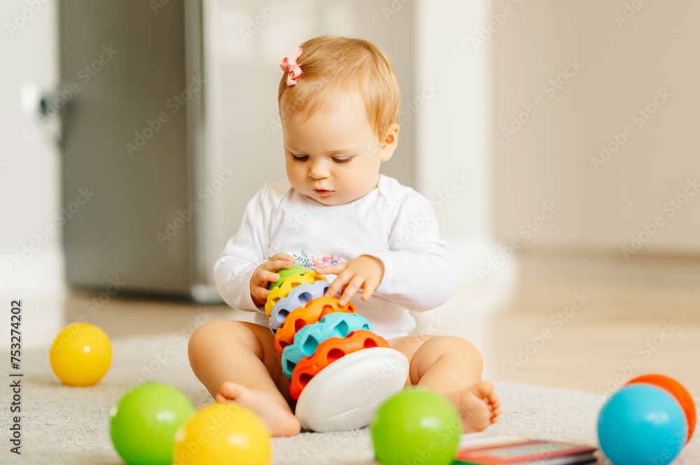 Concentrated sitting on the floor baby girl is playing with colourful toys at home. Concentrated sitting on the floor baby girl is playing with colourful toys at home.