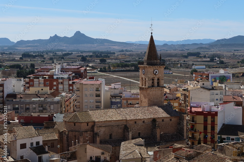 Villena, Alicante, Spain, March 5, 2024: Building and Bell Tower of the Church of Santa Maria with mountains in the background. Villena, Alicante, Spain
