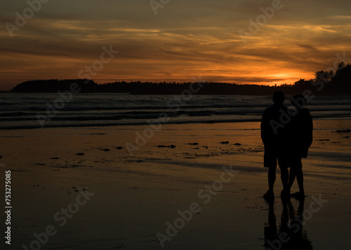 A young couple admiring the stunning orange sunset on a beach in Tofino, Vancouver Island, BC.