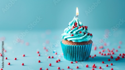 A festive blue cupcake adorned with red sprinkles and a brightly lit candle