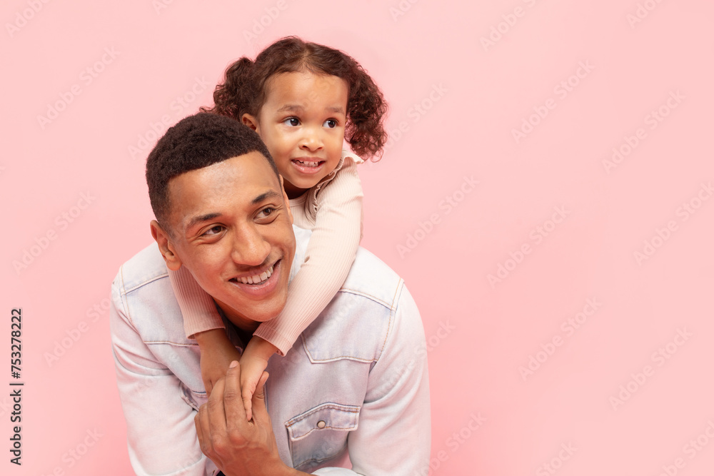 Portrait of happy black father and little daughter embracing, cute child girl cuddling daddy from the back and looking together aside at free space Portrait of happy black father and little daughter embracing, cute child girl cuddling daddy from the back and looking together aside at free space