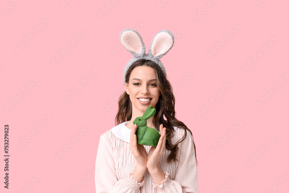 Happy young woman in Easter bunny ears headband with toy rabbit on pink background Happy young woman in Easter bunny ears headband with toy rabbit on pink background