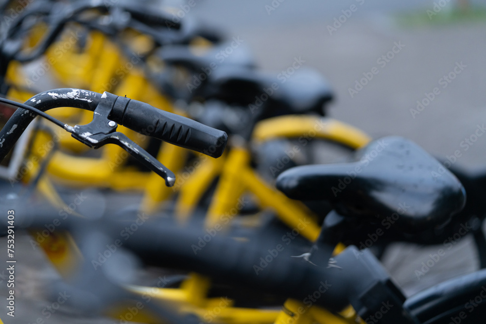 A row of yellow rental bikes lined up along a city sidewalk. A row of yellow rental bikes lined up along a city sidewalk.