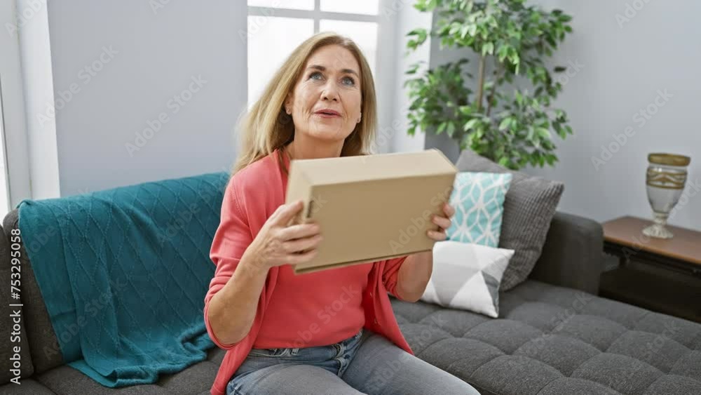 Mature caucasian woman unwrapping package in a cozy living room with a joyful expression. Mature caucasian woman unwrapping package in a cozy living room with a joyful expression.