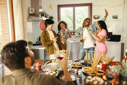Fotografía Cheerful young group of diverse friends holding drinks and dancing at home kitch