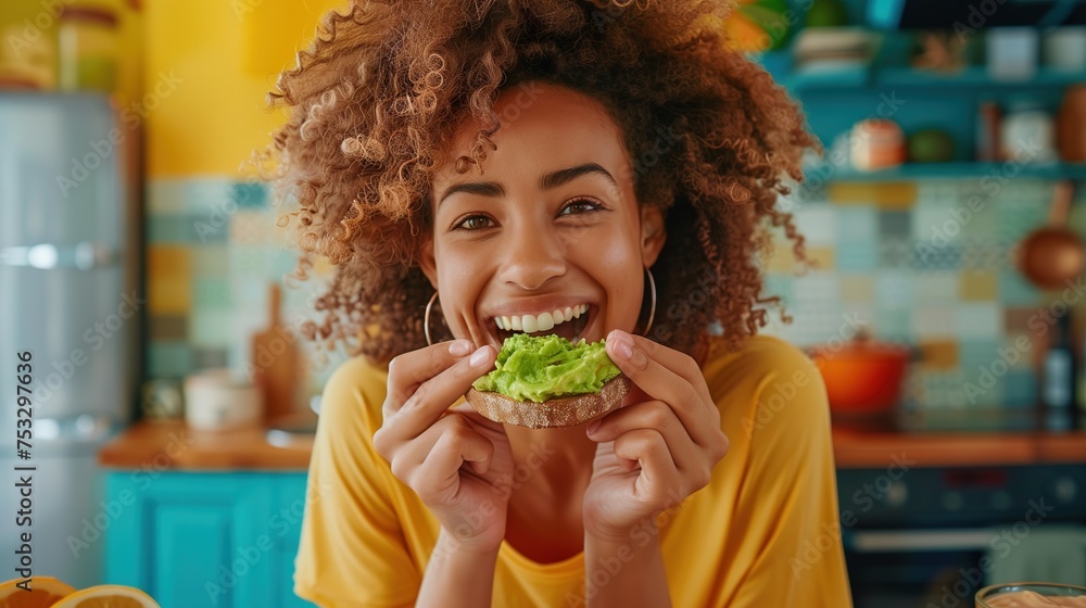a woman happily eating smashed avocado on toast in a colourful kitchen - obrazy, fototapety, plakaty 